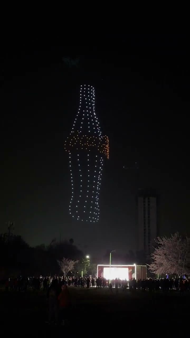 Enjambre de drones formando el contorno de una botella sobre el público de un evento nocturno