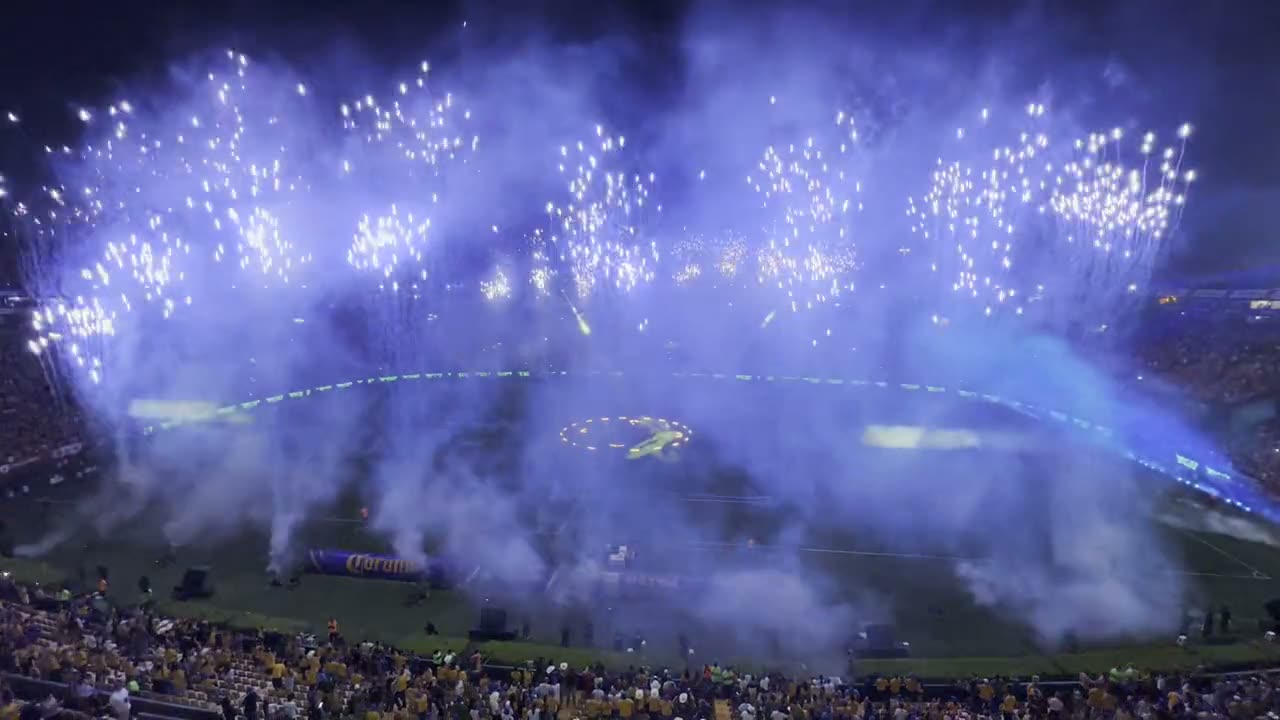 Vista aérea de un estadio lleno con pirotecnia dorada y azul disparada desde el campo